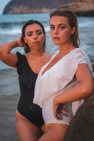 A beautiful Caucasian lesbian couple in swimsuits posing on the beach with the sea in the backgroundの写真素材