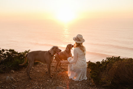 A closeup shot of a young female with two Weimaraner dogs on a seashore