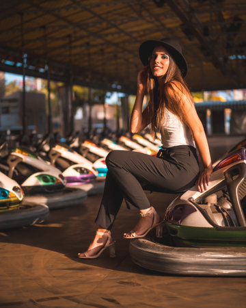 A beautiful brunette female in a black hat posing in an amusement park among bumper carsの写真素材