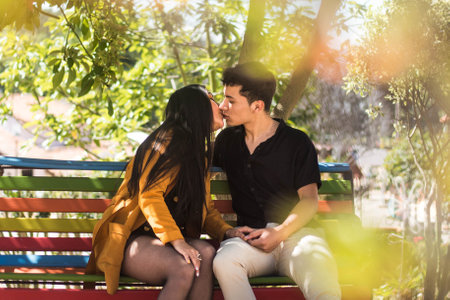 A shallow focus shot of a young couple kissing on a colorful bench outdoorsの写真素材