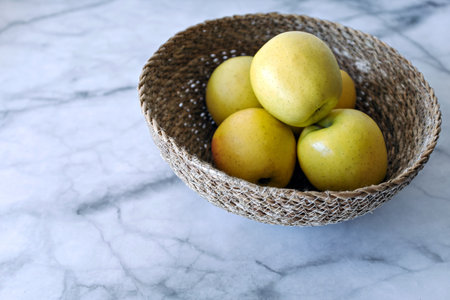 A closeup shot of a wicker bowl with yellow applesの写真素材