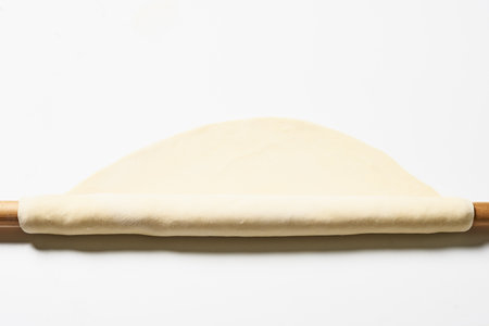 A closeup shot of a rolled out yeast dough with a dough roller on a white surfaceの写真素材