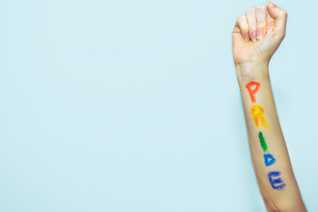 A female's raised fist with a "PRIDE" writing on her arm in gay pride flag colorsの写真素材