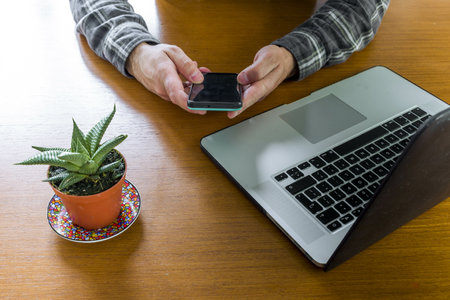 A top-view of a man's hands browsing the phone in the workplace