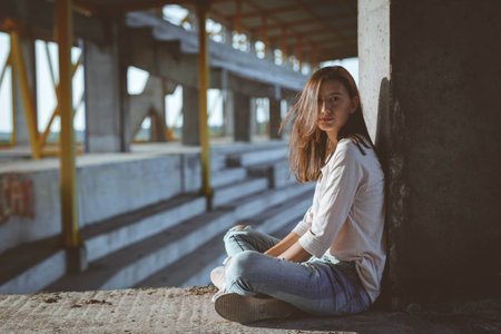 A young caucasian female sitting under the column of a building with unfinished constructionの写真素材