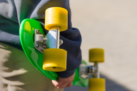 A young girl in a blue sweatshirt holding  a green skateboard with yellow wheels with her armの写真素材