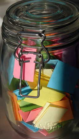 A vertical shot of a jar of positivity with multi-colored handwritten notes inside