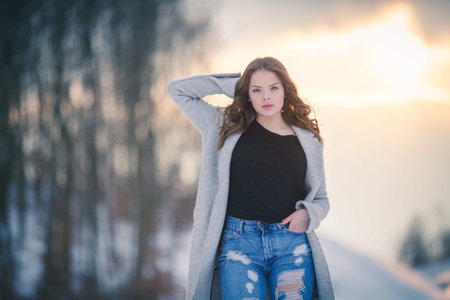 A portrait of an adult woman with long brunette hair wearing jeans with a cardigan in a forest covered in the snowの写真素材