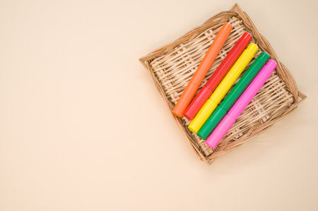 A closeup shot of colorful markers on a small woven tray isolated on a pink backgroundの写真素材