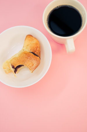 A vertical shot of a cup of coffee and bitten croissant on a white plate isolated on pink background