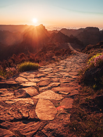 A narrow stone footpath on the hill with high rough mountains in the background during a warm sunsetの写真素材