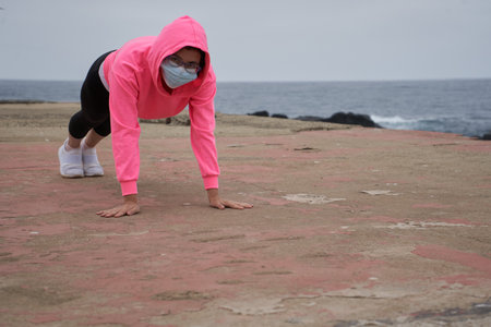 A Chilean woman with a mask doing push-ups in front of the sea - New normality, sport during...