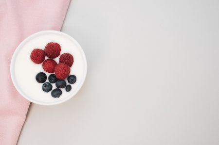 A closeup shot of a ceramic bowl of white yogurt with blueberries and raspberriesの写真素材