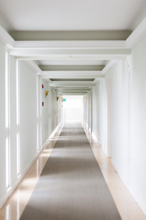 A vertical shot of a long, white corridor with clean walls and reflective floorの写真素材