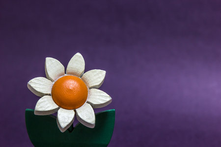 A closeup shot of an artificial wooden flower against a purple background