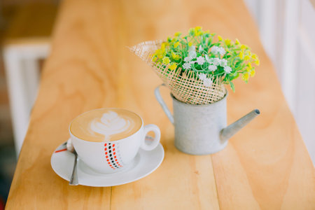 A cup of fresh cappuccino and small beautiful flowers on the cafe table; it's time for coffeeの写真素材