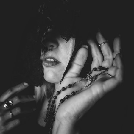 A grayscale shot of a woman with a covered face wearing many rings and holding beads