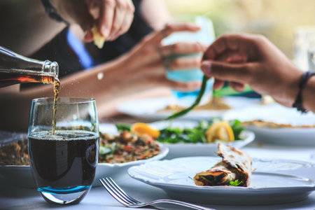 A closeup shot of a drink being poured into a glass and people at the table eating