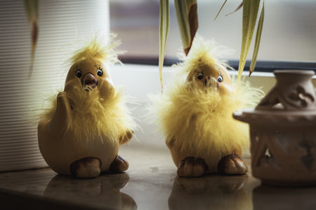 A shot of two yellow chicken chick toys on a windowsill under the home-grown plant.の写真素材