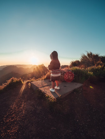 A little child from the back standing on the stone and looking at beautiful sunset and hillsの写真素材