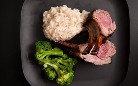 gourmet rack of lamb, chops with risotto and vegetables on a black backgroundの写真素材