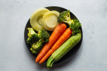 A top view of steamed vegetables on a black plate on a white surfaceの写真素材