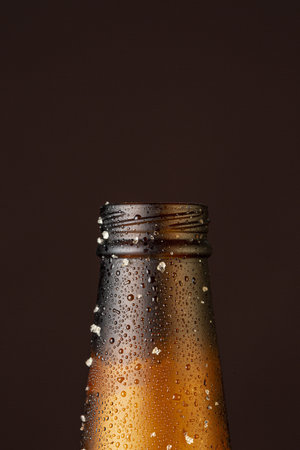 A vertical shot of the rim of an opened beer bottle with drops of liquid spurting out of itの写真素材