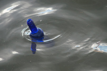 A blue glass bottle floats on the Main towards the Altlantic. No plastic bottle, but still a symbol of our garbage culture. Bad bottle message.の写真素材