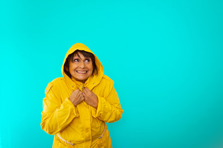An excited senior female wearing a yellow raincoat isolated on blue backgroundの写真素材