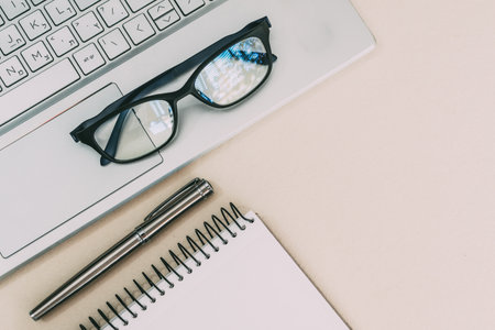A top view closeup of a laptop, notebook, a pen and glasses on the white deskの写真素材