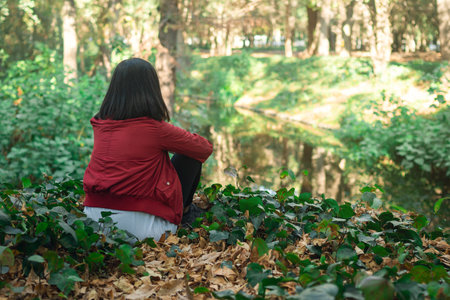 A closeup of a brunette girl sitting on the ground, near a lake in a park during daylightの写真素材