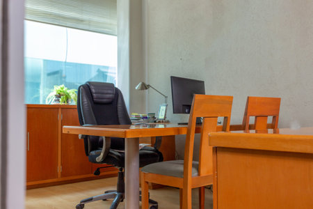 An inside view of a wooden desk with a monitor, leather chair, and a bookshelf in a CEO rooの写真素材