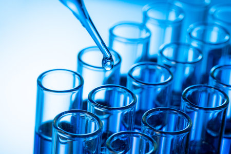 A closeup shot of a pipette tip with a droplet over glass test tubesの写真素材