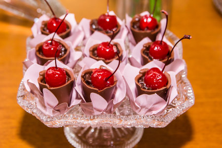 A closeup shot of chocolate cups with red shiny cherries served in a vase on a wooden tableの写真素材