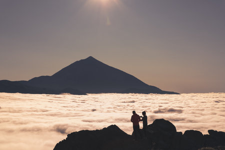 A silhouette shot of a couple on a rocky cliff with a sea of clouds backgroundの写真素材