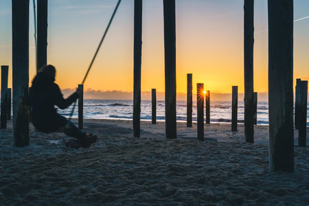 A silhouette of a woman sitting on a swing and enjoying a wonderful view of sunset over a seaの写真素材