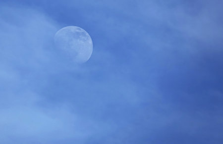 The moon visible during daytime with clouds around blue skyの写真素材