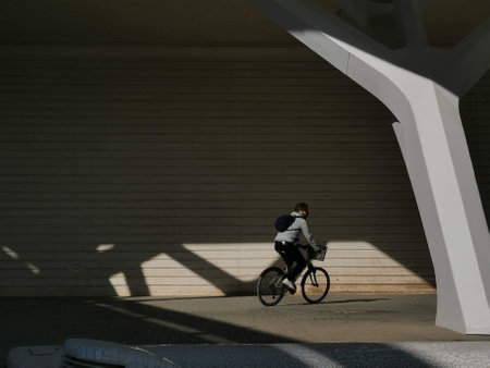 A side view of a young man with a backpack riding a bicycle on a city sidewalkの写真素材