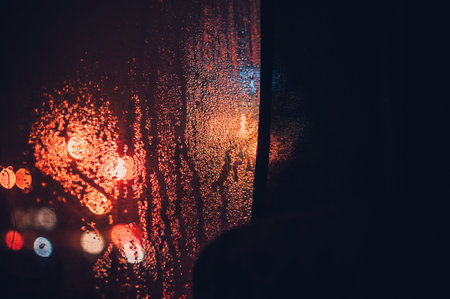 A closeup of a window covered in raindrops with a dark blurred background and bokeh lightsの写真素材