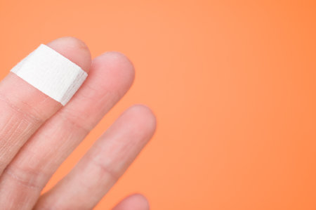 A closeup of a bandage on a finger isolated on an orange backgroundの写真素材