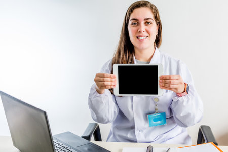 A young professional female doctor sitting in her consulting room showing a blank screen of a tabletの写真素材