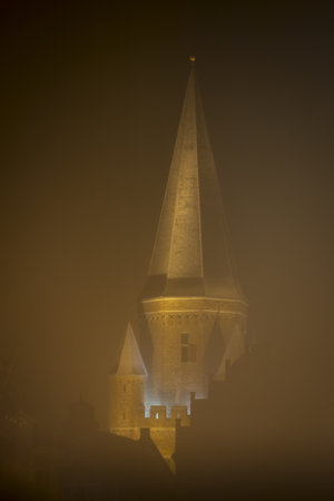 Long exposure with mist from snowfall obscuring the golden glowing Drogenap historic medieval city entrance gate tower rising above silhouetted old buの写真素材