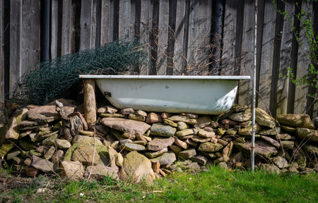 An old tub on a pile of rocks in front of a wooden fence in a backyardの写真素材
