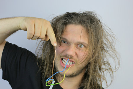 A funny Serbian man holding an electrical cable after getting an electric shock at homeの写真素材