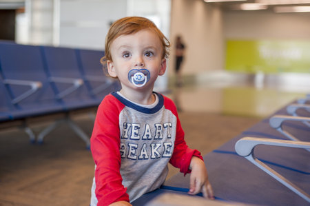 A Caucasian male toddler standing in front of chairs in the waiting a
