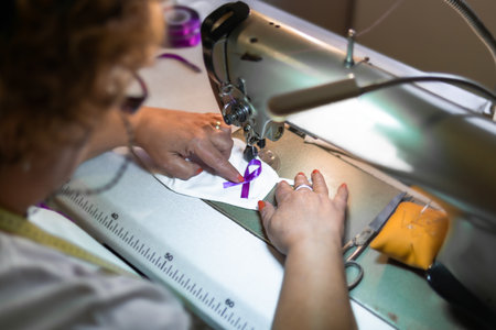 An adult female sewing a purple ribbon on a facemask in the workshop - COVID-19 awarenessの写真素材
