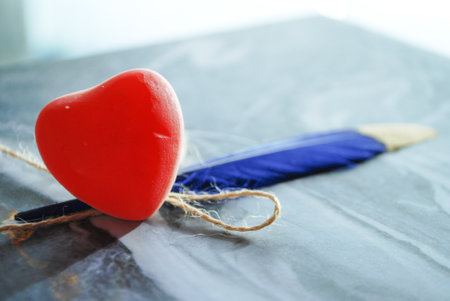 red jelly heart with blue feather isolated on marbled wavy paper,daylight blurry background,romantic wallpaper,space for qoutes and textの写真素材