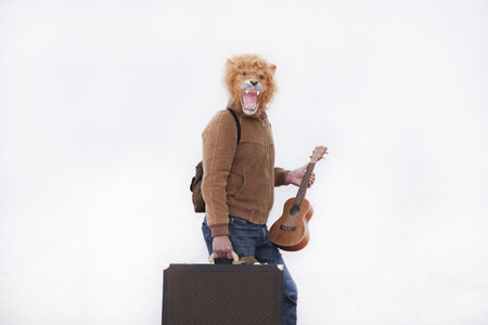 A man with a roaring lion full mask with a brown briefcase and ukulele isolated on white backgroundの写真素材