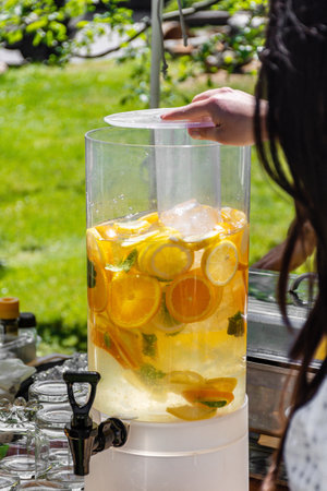Selective focus of person preparing refreshing beverage with slices of citrus fruits in large water dispenser with tap.の写真素材