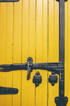 A vertical shot of a yellow door with a metal lockの写真素材
